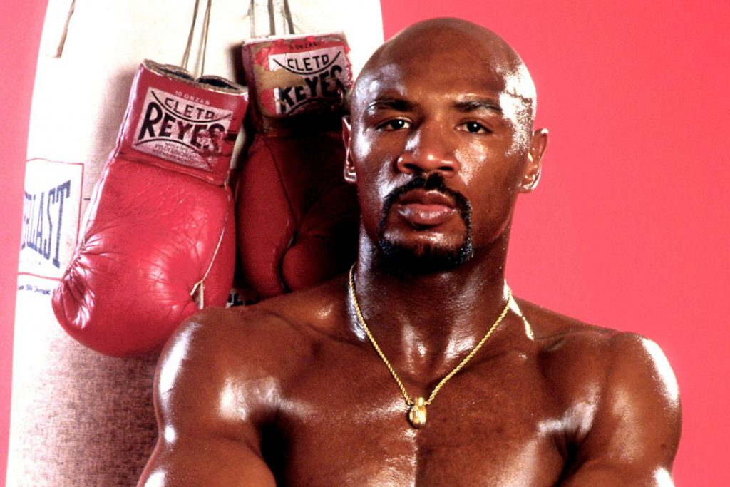 Marvin Hagler posando para foto com luvas de boxe atrás dele.